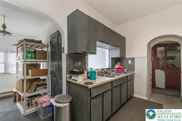 kitchen featuring baseboard heating, light countertops, decorative backsplash, arched walkways, and a sink