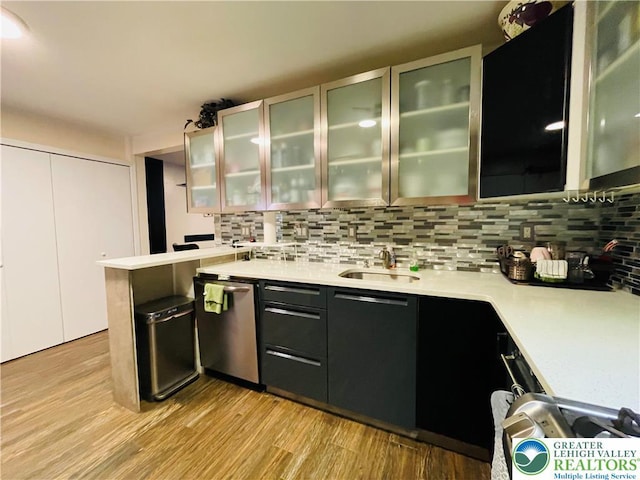 bar area featuring a sink, decorative backsplash, stainless steel dishwasher, and light wood-type flooring