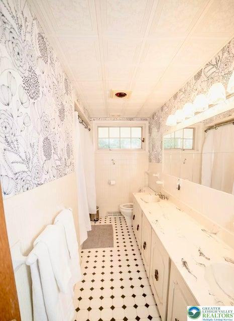 71 Dogwood Dr, Penn Forest Township, PA 18229 - bathroom featuring a shower with shower curtain, double vanity, wallpapered walls, toilet, and a sink