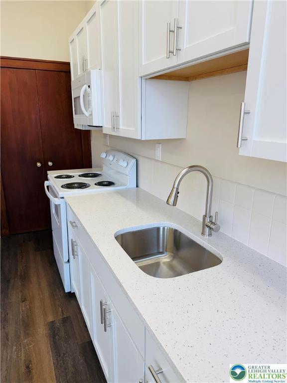 kitchen featuring white appliances, dark wood-style floors, white cabinetry, light stone countertops, and a sink