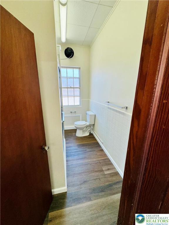 bathroom featuring toilet, wood finished floors, ornamental molding, and a wainscoted wall