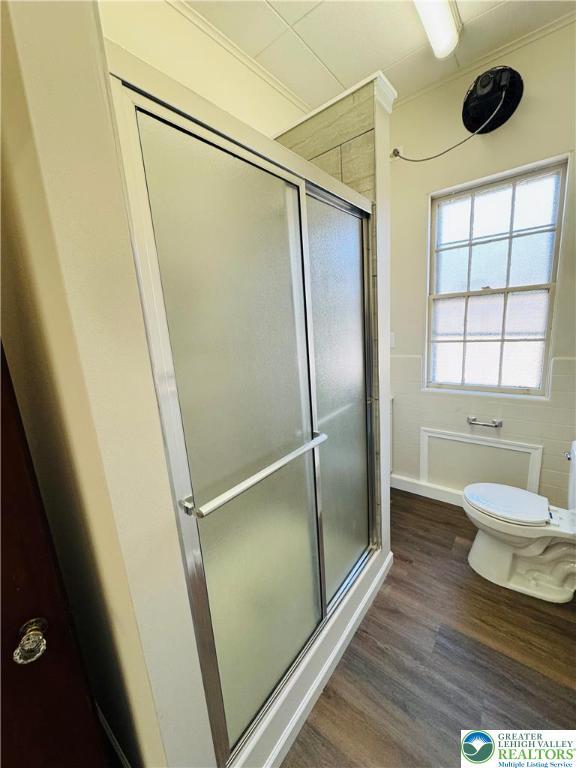 bathroom with a shower stall, crown molding, wood finished floors, and toilet