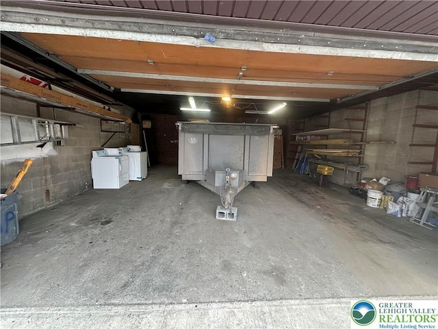 garage featuring washing machine and clothes dryer and concrete block wall