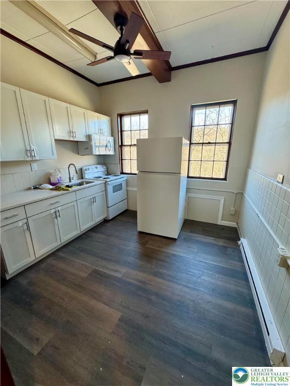 kitchen featuring baseboard heating, white appliances, a ceiling fan, white cabinets, and a sink