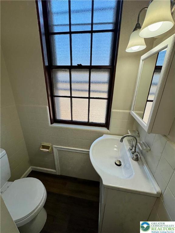 half bath with vanity, a wainscoted wall, toilet, tile walls, and wood finished floors