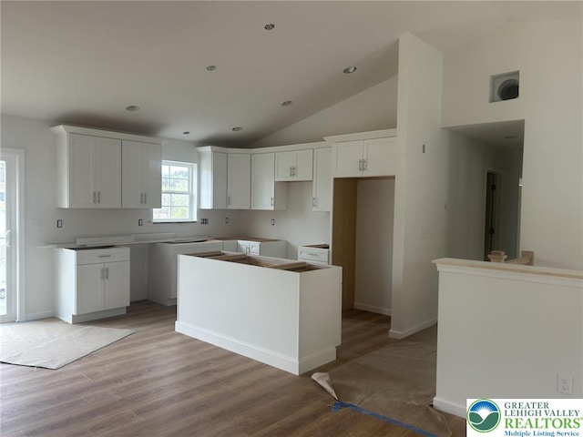 kitchen featuring white cabinets, light wood finished floors, a center island, baseboards, and lofted ceiling