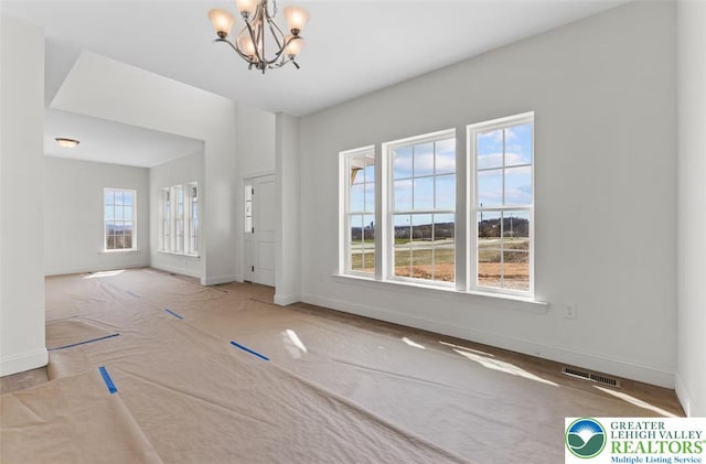 spare room with a chandelier, carpet, visible vents, and baseboards
