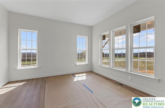 spare room featuring baseboards, wood finished floors, and visible vents
