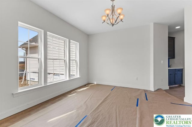 unfurnished dining area with baseboards, a notable chandelier, and light colored carpet