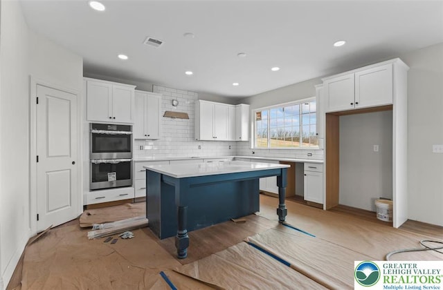 kitchen featuring white cabinets, backsplash, stainless steel double oven, and visible vents