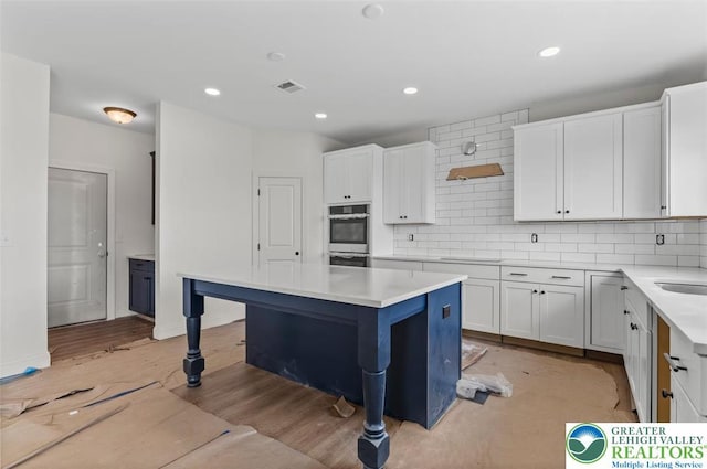 kitchen with white cabinets, stainless steel double oven, light countertops, and decorative backsplash
