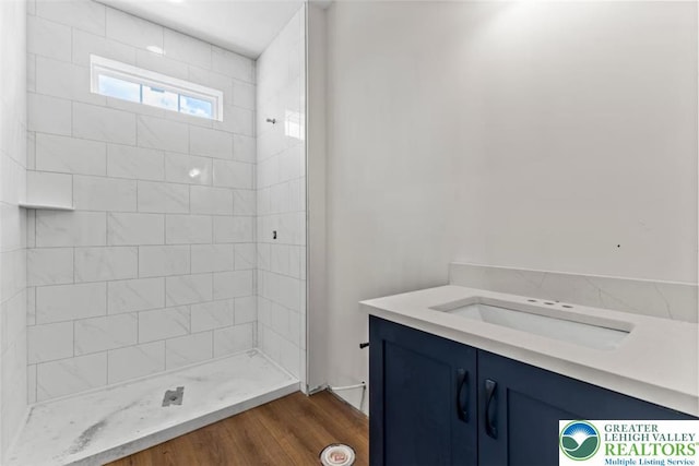 full bathroom featuring a tile shower, wood finished floors, and vanity