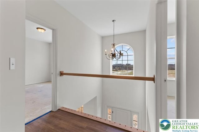 hall with a notable chandelier, wood finished floors, and an upstairs landing