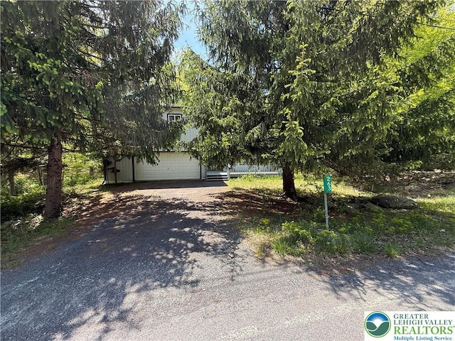obstructed view of property with dirt driveway, a garage, and an outdoor structure