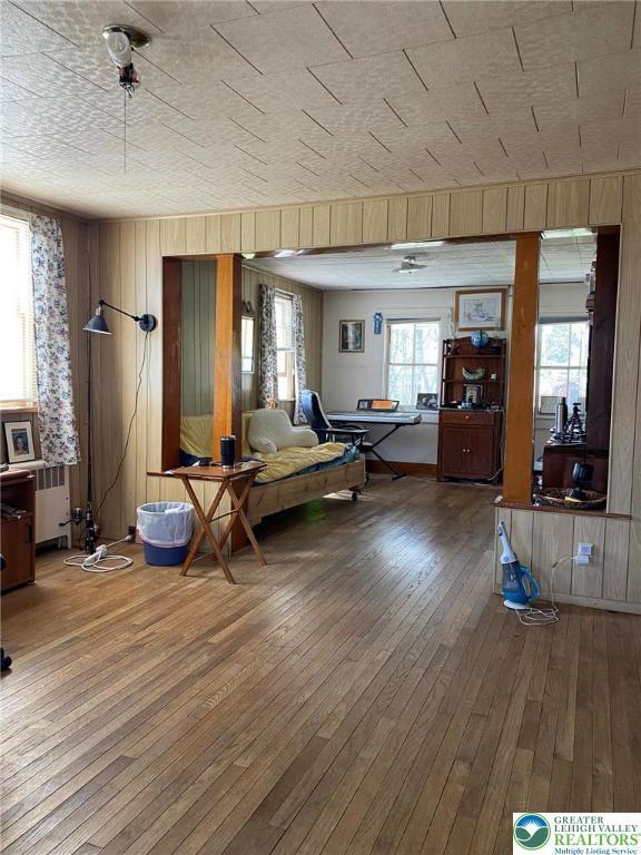 living area with wood-type flooring, radiator heating unit, and wooden walls