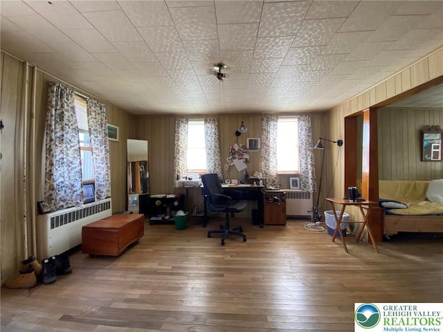 home office with radiator heating unit, hardwood / wood-style floors, and wooden walls