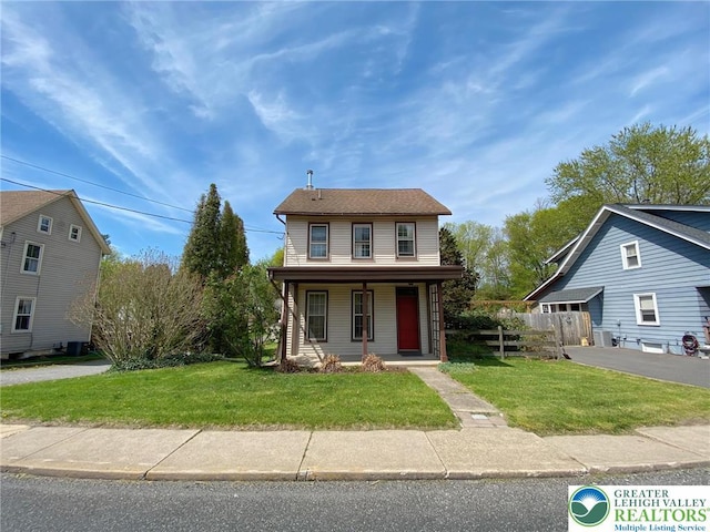 traditional home with a porch, a front lawn, and fence