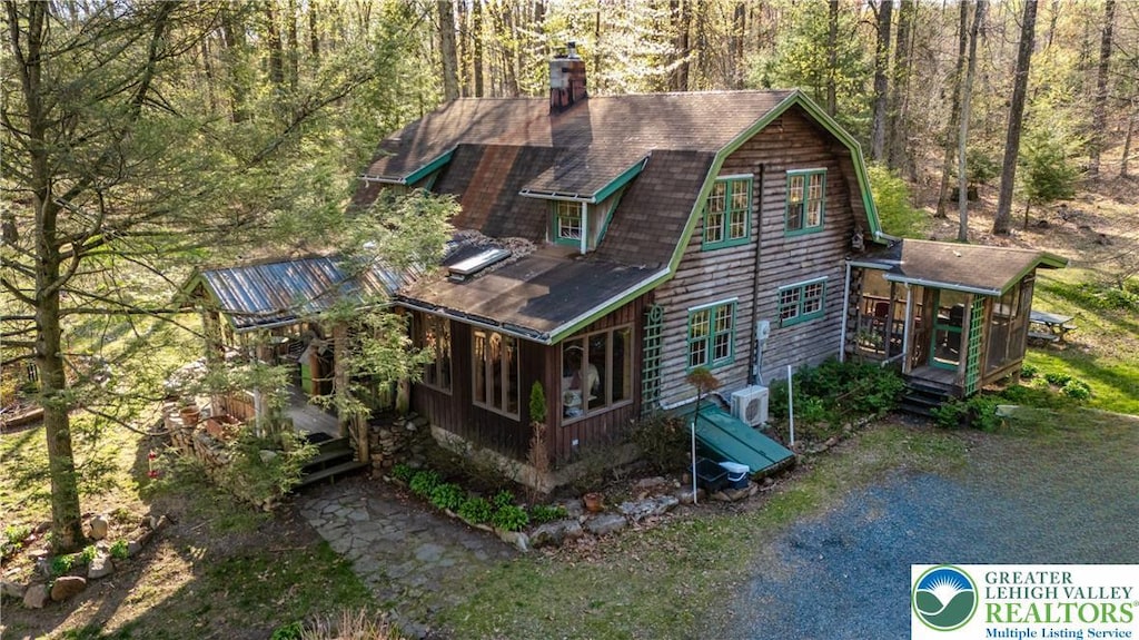 exterior space with a gambrel roof, a view of trees, a deck, and a sunroom