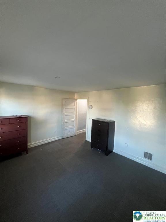 unfurnished room featuring baseboards, dark colored carpet, and visible vents