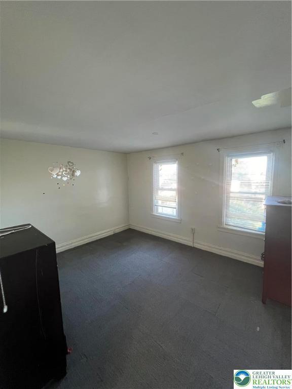 unfurnished room featuring baseboards and dark colored carpet