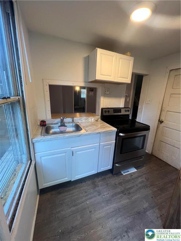 kitchen with dark wood finished floors, light countertops, a sink, stainless steel electric range, and white cabinetry