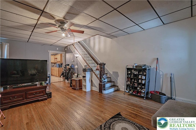 living room featuring stairway, hardwood / wood-style flooring, a ceiling fan, and a paneled ceiling