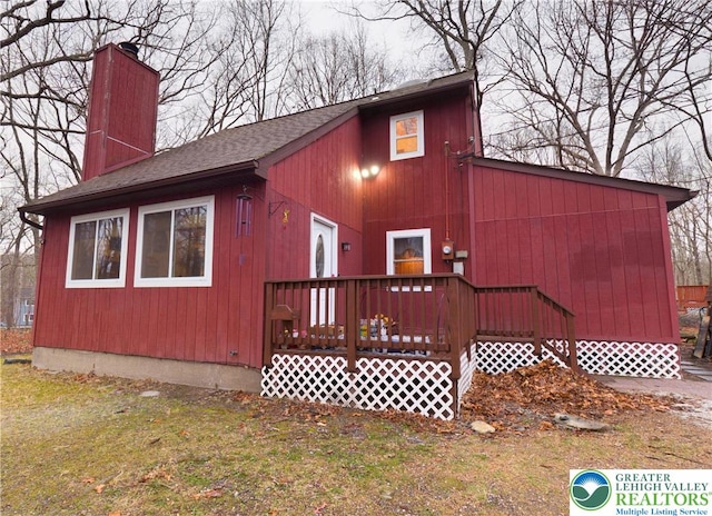 view of front of home with a wooden deck, roof with shingles, and a chimney