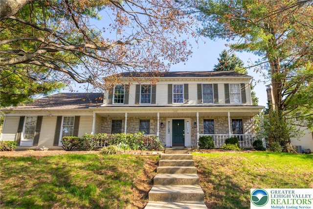 colonial house featuring a front yard, a porch, and stone siding