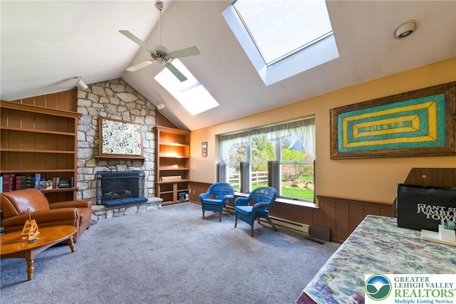 carpeted living room featuring ceiling fan, a stone fireplace, built in features, and wainscoting
