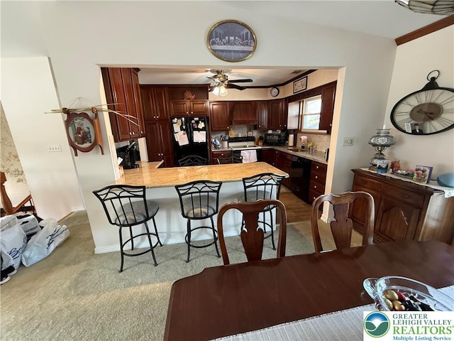 kitchen with black appliances, a ceiling fan, a peninsula, light countertops, and carpet floors