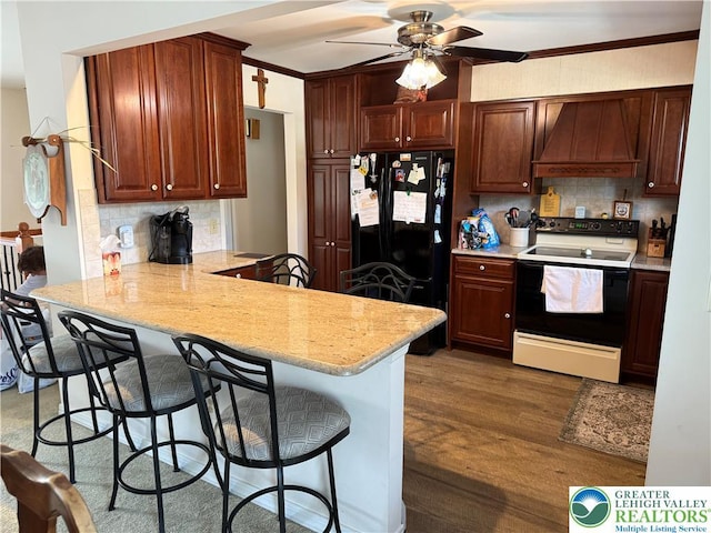kitchen featuring electric stove, freestanding refrigerator, backsplash, a peninsula, and premium range hood