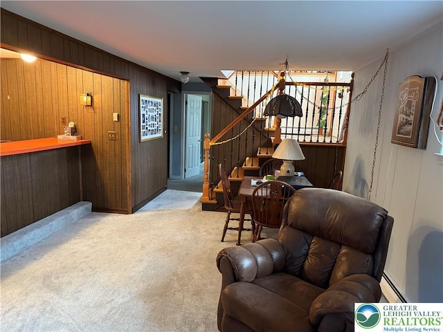 carpeted living room featuring a baseboard heating unit, stairs, and wooden walls
