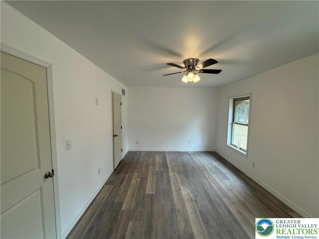 spare room featuring ceiling fan, visible vents, dark wood finished floors, and baseboards