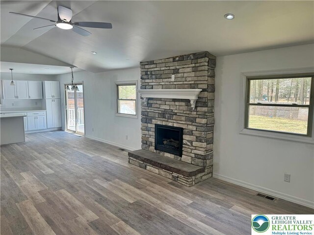 unfurnished living room featuring visible vents, ceiling fan, baseboards, light wood-type flooring, and a stone fireplace