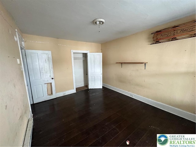 unfurnished bedroom with baseboards, a closet, and dark wood-type flooring