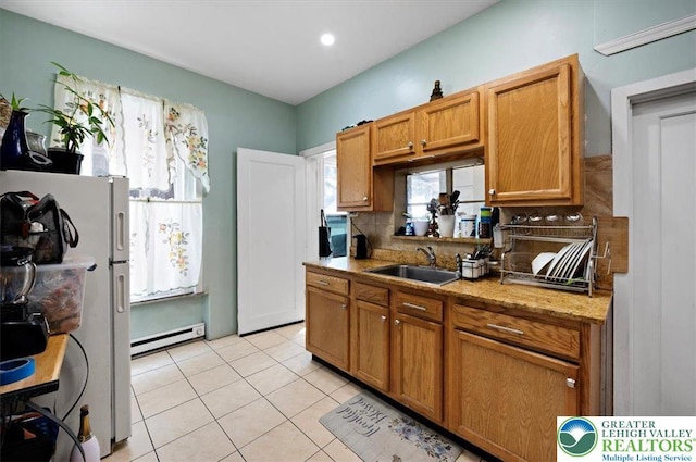 kitchen with a sink, decorative backsplash, light tile patterned floors, baseboard heating, and freestanding refrigerator