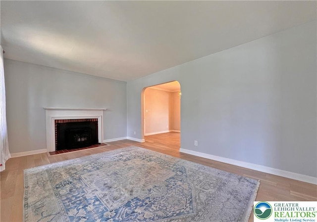 unfurnished living room with a brick fireplace, wood finished floors, baseboards, and arched walkways