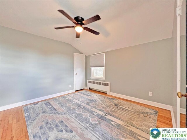 unfurnished bedroom featuring wood finished floors, radiator heating unit, baseboards, a ceiling fan, and lofted ceiling
