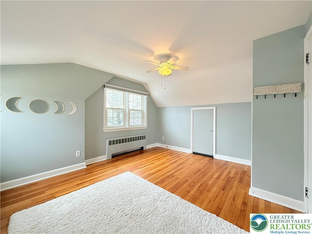 bonus room featuring light wood-style floors, vaulted ceiling, radiator, ceiling fan, and baseboards