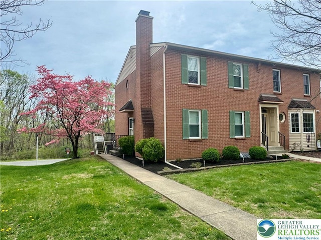 view of front of property featuring a chimney, a front yard, and brick siding