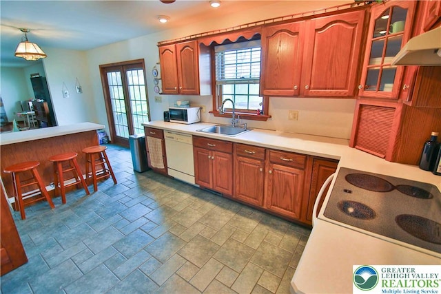 kitchen with glass insert cabinets, under cabinet range hood, light countertops, dishwasher, and a sink