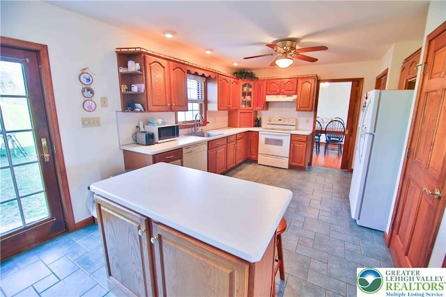 kitchen featuring a sink, under cabinet range hood, open shelves, brown cabinetry, and white appliances