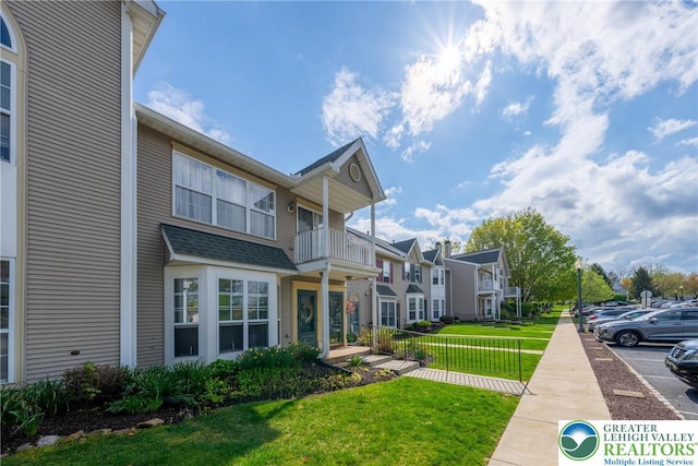 exterior space featuring uncovered parking, a balcony, a residential view, a lawn, and fence