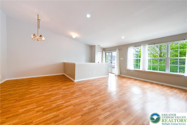 empty room featuring baseboards, a notable chandelier, light wood-style flooring, and vaulted ceiling