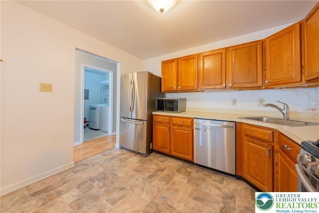 kitchen featuring a sink, brown cabinets, stainless steel appliances, stone finish flooring, and washer / clothes dryer