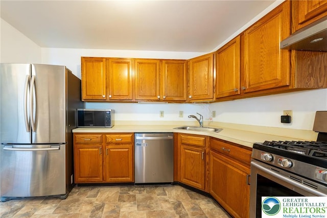kitchen with a sink, brown cabinets, stainless steel appliances, under cabinet range hood, and stone finish flooring