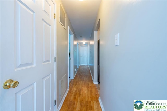 hall with visible vents, baseboards, and light wood-style floors