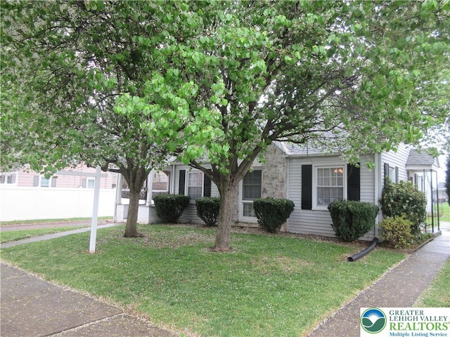 view of property hidden behind natural elements with fence, a front lawn, and stone siding