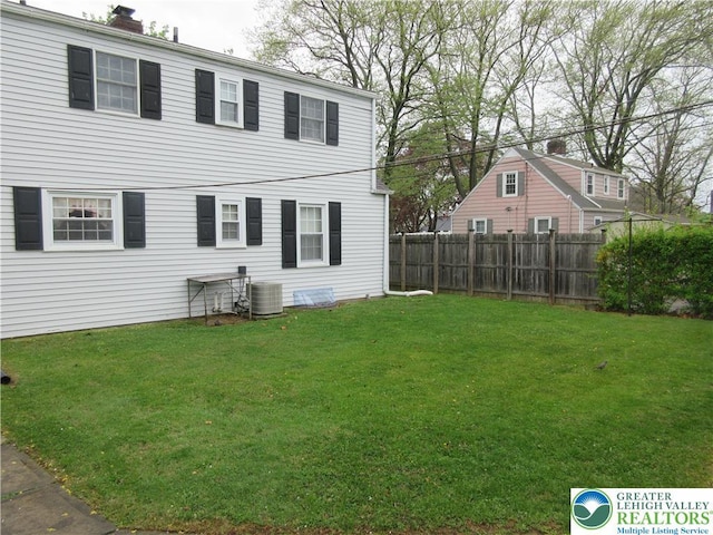 rear view of house featuring a chimney, fence, and a yard
