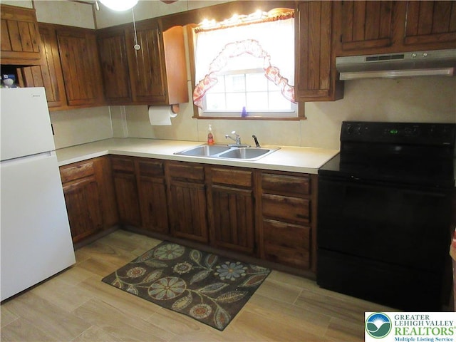 kitchen featuring a sink, under cabinet range hood, black electric range oven, light countertops, and freestanding refrigerator